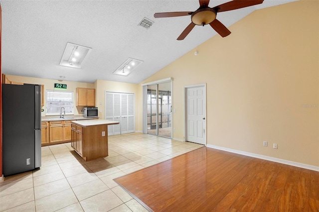 kitchen with visible vents, a sink, a kitchen island, freestanding refrigerator, and light countertops