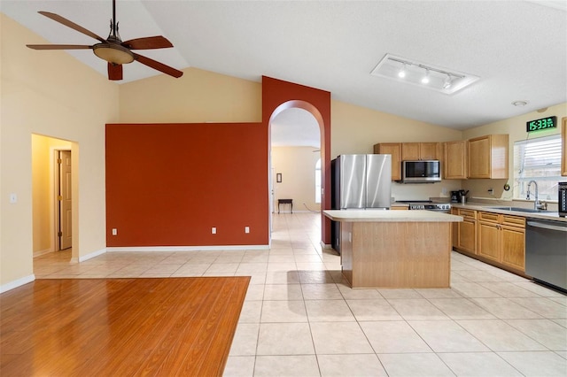 kitchen with a sink, a kitchen island, stainless steel appliances, arched walkways, and light countertops