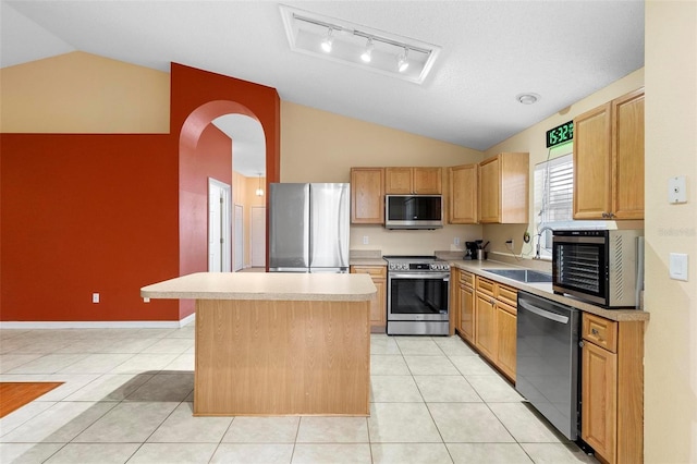 kitchen with a sink, a kitchen island, stainless steel appliances, light tile patterned flooring, and vaulted ceiling