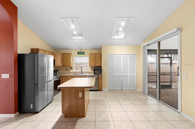 kitchen featuring light countertops, vaulted ceiling, light tile patterned flooring, stainless steel appliances, and a sink