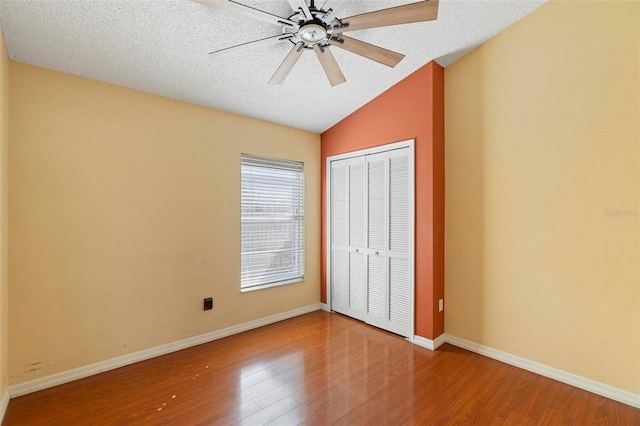 unfurnished bedroom with vaulted ceiling, wood finished floors, a closet, and a textured ceiling