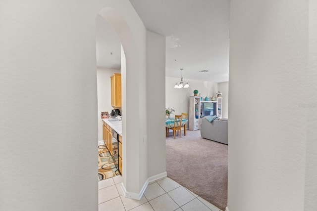 hall with baseboards, light colored carpet, light tile patterned floors, arched walkways, and a notable chandelier