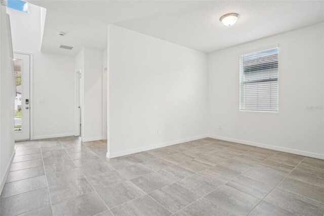 empty room with visible vents, a wealth of natural light, and baseboards