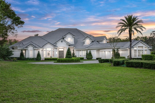 french country inspired facade featuring stucco siding, a tiled roof, and a front yard