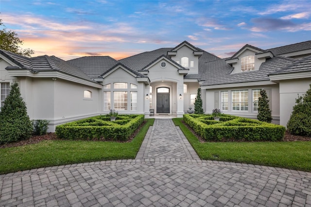 view of front facade featuring a tile roof, a lawn, and stucco siding