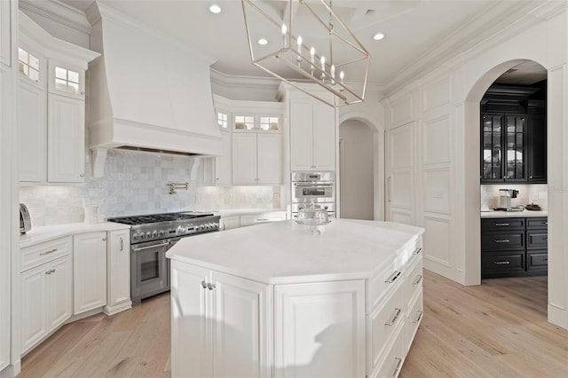 kitchen with ornamental molding, arched walkways, premium range hood, and stainless steel appliances