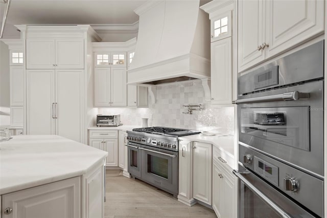 kitchen with custom exhaust hood, ornamental molding, stainless steel appliances, light countertops, and backsplash