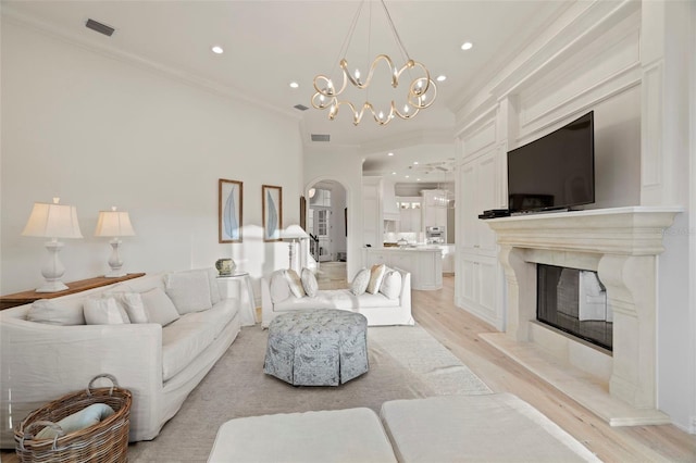 living room featuring visible vents, a notable chandelier, light wood-style flooring, a high end fireplace, and crown molding