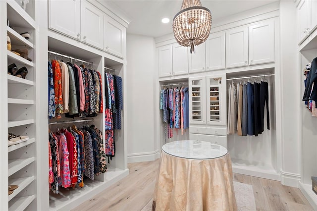 walk in closet with light wood-style flooring and an inviting chandelier