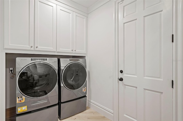 clothes washing area with light wood-style flooring, cabinet space, baseboards, and washing machine and clothes dryer