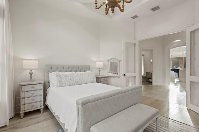 bedroom with an inviting chandelier, arched walkways, visible vents, and light wood finished floors