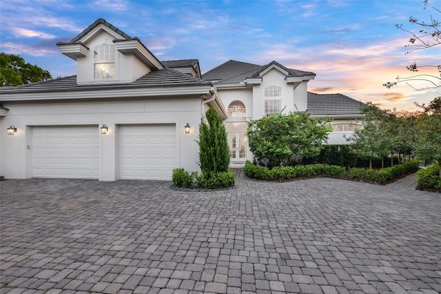 view of front of home with stucco siding, decorative driveway, french doors, a garage, and a tiled roof