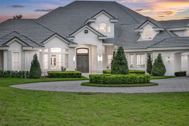 french country style house featuring stucco siding, a lawn, and a tile roof