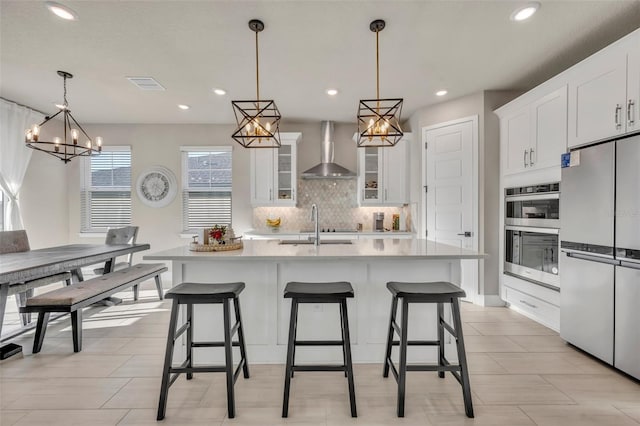 kitchen featuring visible vents, freestanding refrigerator, double oven, an inviting chandelier, and wall chimney exhaust hood