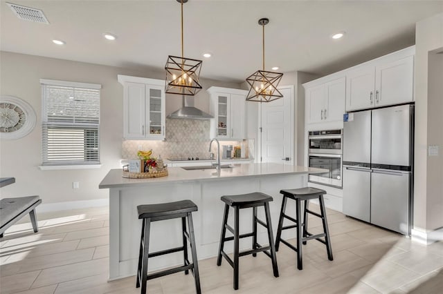 kitchen featuring visible vents, backsplash, white cabinetry, appliances with stainless steel finishes, and wall chimney exhaust hood