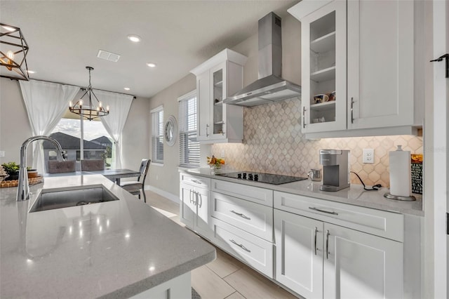 kitchen featuring black electric stovetop, a chandelier, decorative backsplash, wall chimney exhaust hood, and a sink