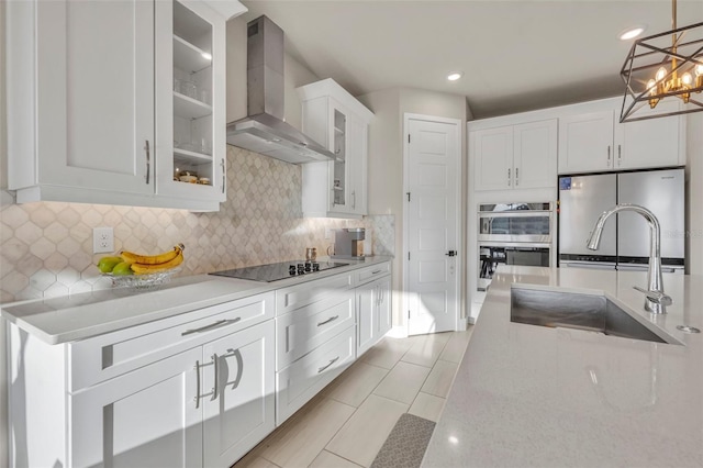 kitchen featuring a sink, appliances with stainless steel finishes, wall chimney exhaust hood, white cabinets, and hanging light fixtures