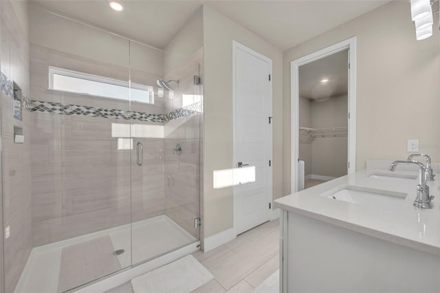 bathroom with a walk in closet, a sink, recessed lighting, a shower stall, and double vanity