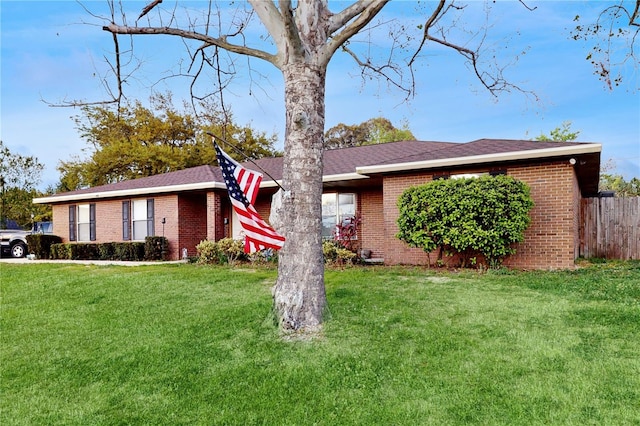 ranch-style home featuring brick siding, a front lawn, and fence