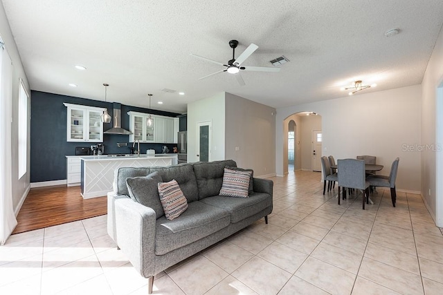 living room with visible vents, a ceiling fan, a textured ceiling, arched walkways, and light tile patterned floors