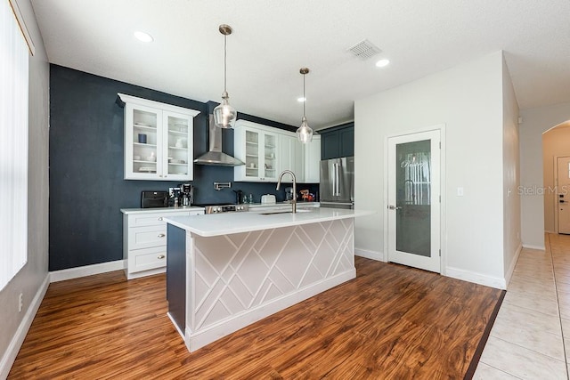 kitchen with arched walkways, a sink, light countertops, appliances with stainless steel finishes, and wall chimney range hood