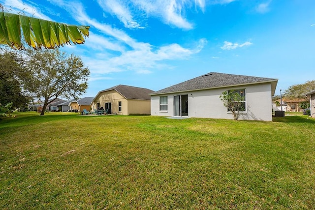 rear view of house featuring a lawn, central AC, and stucco siding