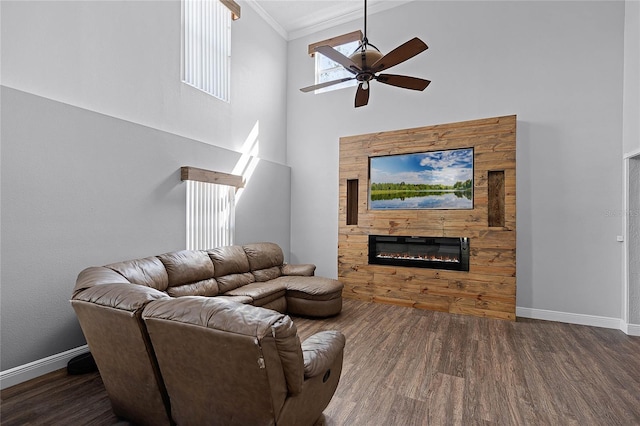 living room featuring ornamental molding, wood finished floors, a glass covered fireplace, baseboards, and ceiling fan