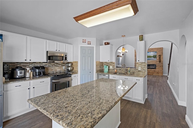 kitchen with a sink, arched walkways, appliances with stainless steel finishes, and white cabinets