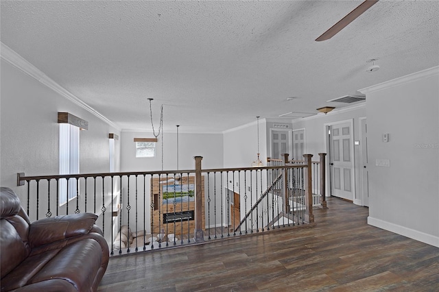 hallway with wood finished floors, baseboards, ornamental molding, a textured ceiling, and an upstairs landing