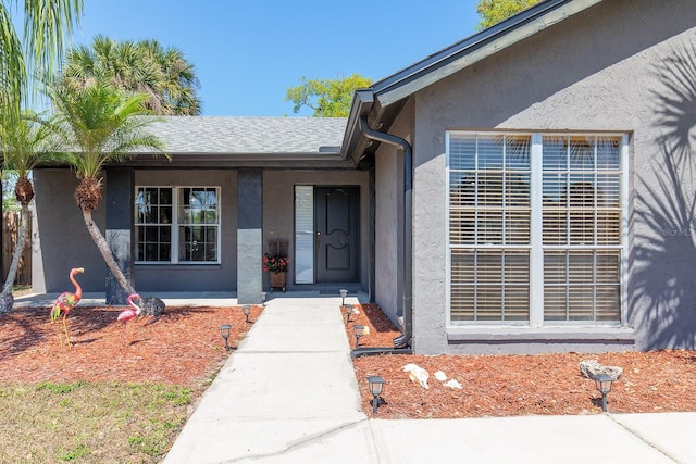 property entrance featuring stucco siding and a shingled roof