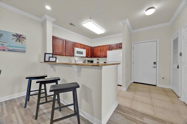 kitchen featuring visible vents, a kitchen bar, ornamental molding, white appliances, and a peninsula