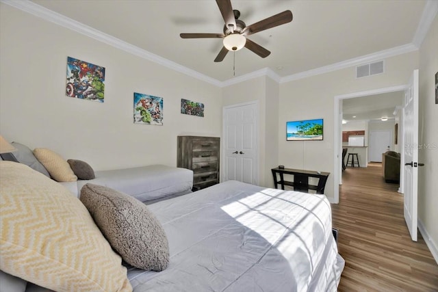 bedroom with visible vents, crown molding, baseboards, wood finished floors, and a ceiling fan