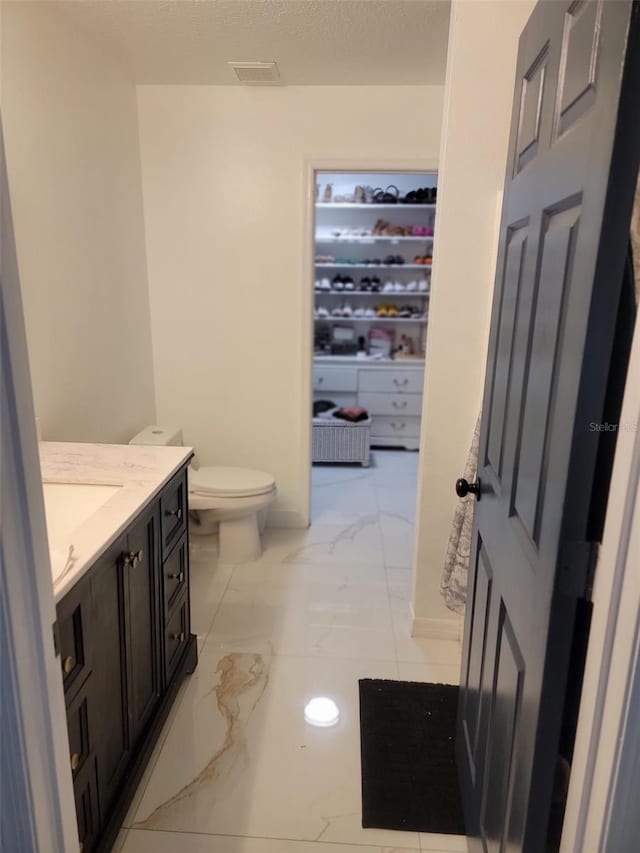 bathroom with visible vents, toilet, vanity, marble finish floor, and a textured ceiling