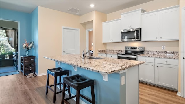 kitchen featuring visible vents, a center island with sink, light wood-style flooring, stainless steel appliances, and a sink