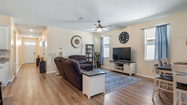 living room with light wood-type flooring, visible vents, a ceiling fan, a textured ceiling, and baseboards