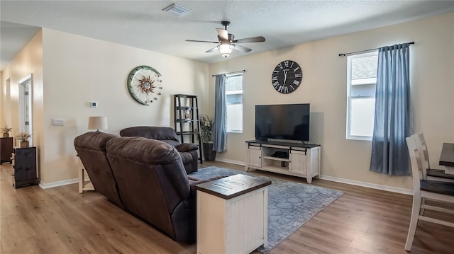 living area with a ceiling fan, wood finished floors, visible vents, baseboards, and a textured ceiling