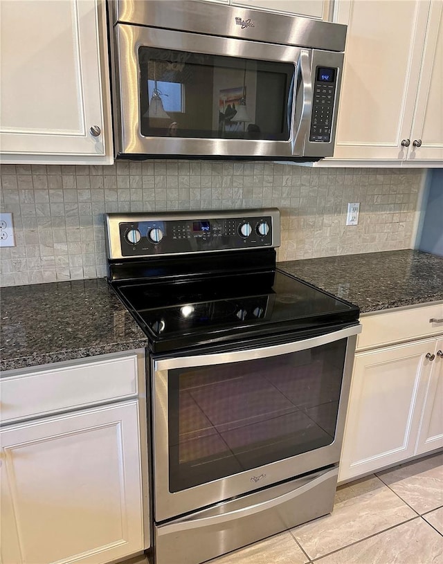 kitchen with tasteful backsplash, white cabinets, appliances with stainless steel finishes, and dark stone counters