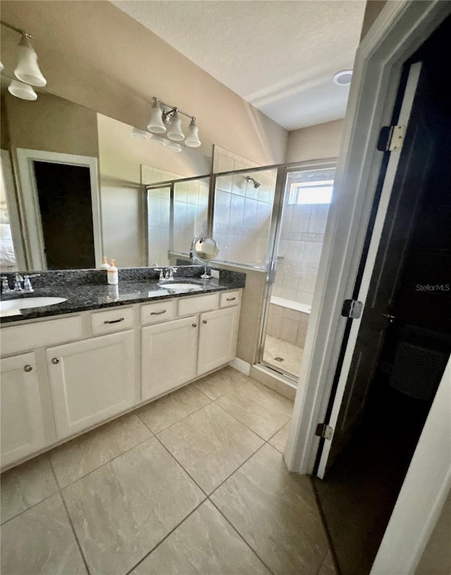 bathroom featuring a sink, a textured ceiling, a stall shower, and double vanity