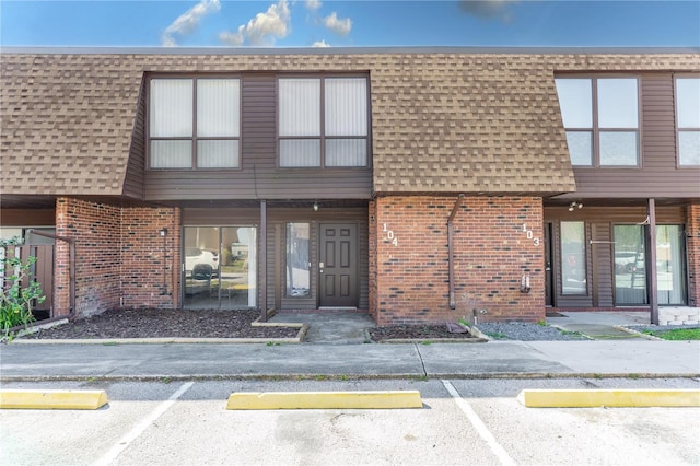 exterior space with brick siding, mansard roof, roof with shingles, and uncovered parking