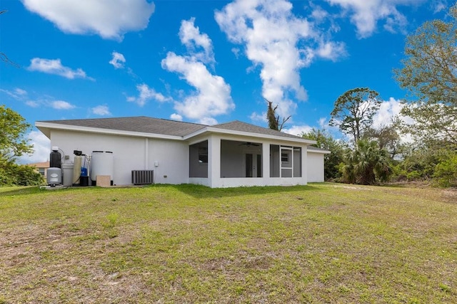 rear view of house with stucco siding, a lawn, a sunroom, central AC unit, and ceiling fan