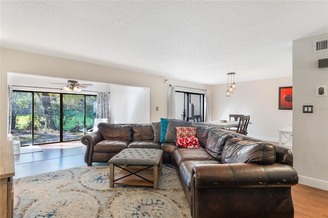 living area featuring visible vents, ceiling fan, baseboards, wood finished floors, and a textured ceiling