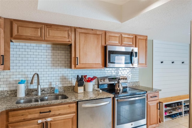 kitchen featuring light stone countertops, a sink, stainless steel appliances, a textured ceiling, and tasteful backsplash