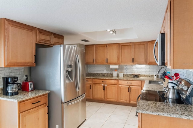 kitchen featuring tasteful backsplash, light stone countertops, stainless steel appliances, a raised ceiling, and a sink