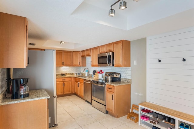 kitchen featuring light tile patterned floors, decorative backsplash, appliances with stainless steel finishes, a raised ceiling, and a sink