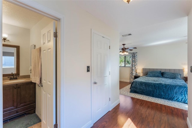 bedroom with visible vents, wood finished floors, baseboards, and a sink