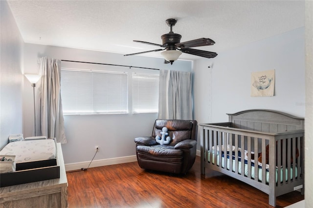 bedroom with wood finished floors, baseboards, ceiling fan, a nursery area, and a textured ceiling