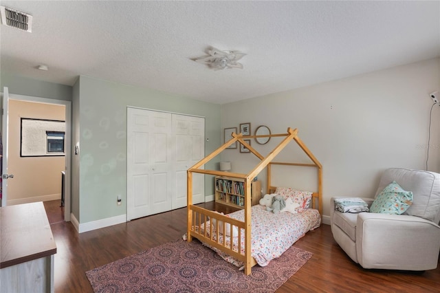 bedroom with wood finished floors, baseboards, visible vents, a closet, and a textured ceiling