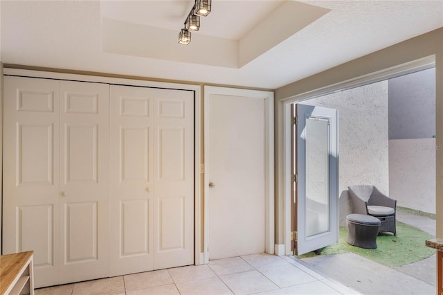 interior space with light tile patterned floors, a closet, a raised ceiling, and track lighting