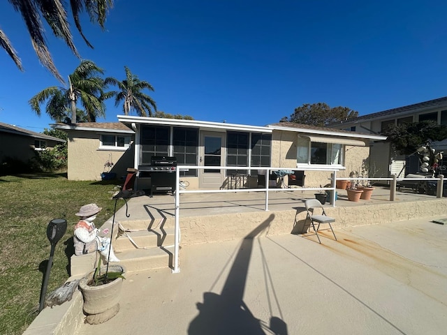 view of front facade featuring stucco siding, a sunroom, a front yard, and a patio area