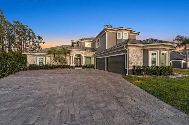 view of front facade featuring stucco siding, a garage, stone siding, a tile roof, and decorative driveway